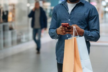 Akıllı telefon kullanıyor. Süpermarketteki alışveriş çantalı adamın yakın görüntüsü..