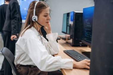 Kulaklıkla, bilgisayarın yanında oturuyor. Tasarımcı takımı ofiste birlikte..