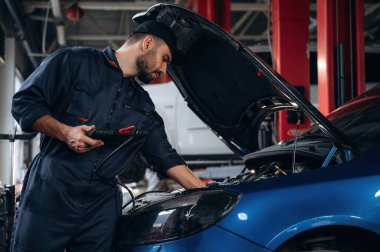 Elinde siyah dijital tablet var. Araba tamirhanesinde çalışan bir tamirci..