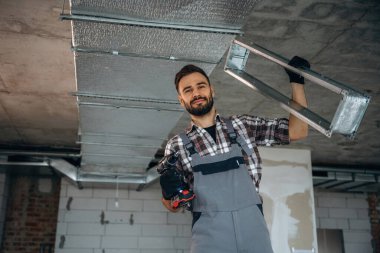 Parçayı tavana yerleştirmeye hazırız. Bir adam bitmemiş bir odayı yeniliyor..