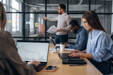 Adam camın yanında duruyor, bilgi veriyor. Profesyonel işçiler modern ofiste birlikte çalışıyorlar..