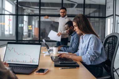 Adam camın yanında duruyor, bilgi veriyor. Profesyonel işçiler modern ofiste birlikte çalışıyorlar..