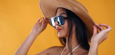 Yan görünüş, ayakta, güneş gözlüğü ve hasır şapkayla. Genç ve güzel bir turist kadın arka plana karşı..