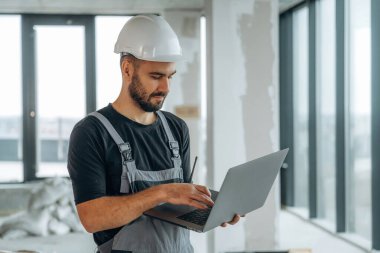 Gümüş renkli dizüstü bilgisayar ellerinde. Bir adam bitmemiş bir odayı yeniliyor..
