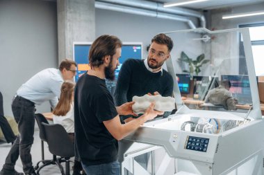 Ayakta. Modern teknoloji. Ofiste 3D yazıcının yanında insanlar var..