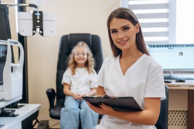 Kadın not defteriyle birlikte. Göz doktoru kliniğinde doktorla küçük bir kız..