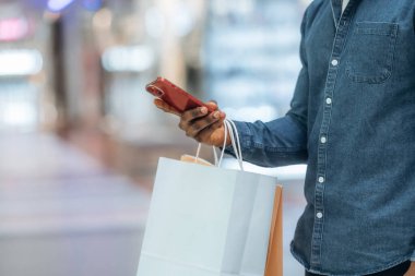 Akıllı telefondan interneti kaydırmak. Süpermarketteki alışveriş çantalı adamın yakın görüntüsü..