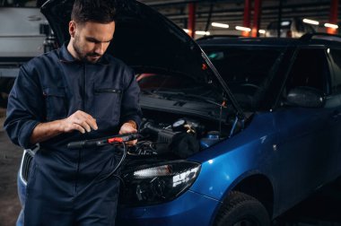 Dijital tablet ellerinde. Araba tamirhanesinde çalışan bir tamirci..