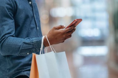 Akıllı telefondan interneti kaydırmak. Süpermarketteki alışveriş çantalı adamın yakın görüntüsü..