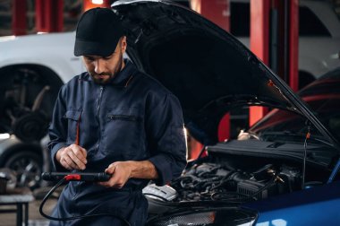 Dijital tablet ellerinde. Araba tamirhanesinde çalışan bir tamirci..