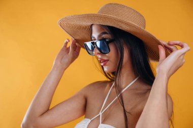 Yan görünüş, ayakta, güneş gözlüğü ve hasır şapkayla. Genç ve güzel bir turist kadın arka plana karşı..