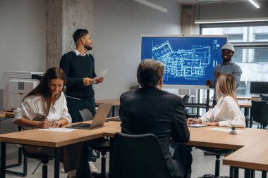 İnşaat planı ekranda. Bir grup ofis çalışanı içeride birlikte..