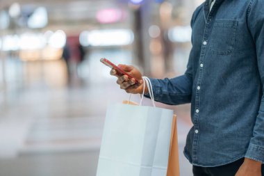 Akıllı telefon kullanıyor. Süpermarketteki alışveriş çantalı adamın yakın görüntüsü..