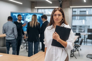 Bir kadının elinde not defteri. Bir grup ofis çalışanı içeride birlikte..