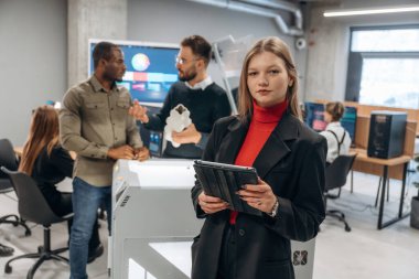 Dijital tablet ellerinde. Ofiste 3D yazıcının yanında insanlar var..