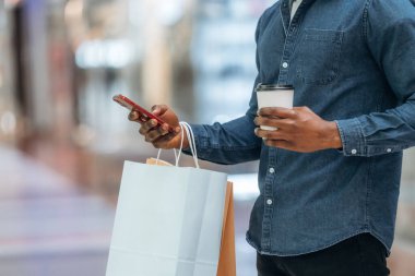 Akıllı telefon kullanıyor. Süpermarketteki alışveriş çantalı adamın yakın görüntüsü..