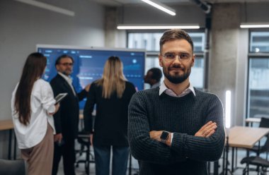 Kollarını kavuşturup meslektaşlarına karşı durarak. Bir grup ofis çalışanı içeride birlikte..