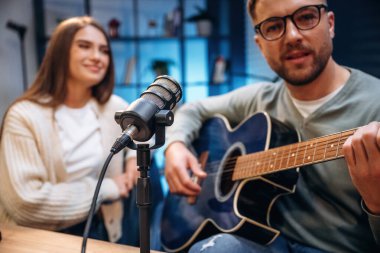 Akustik gitarla. Radyodaki erkek müzisyen kadın sunucuyla podcast yapıyor..