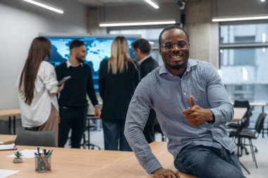 Afrikalı Amerikalı adam meslektaşlarına karşı duruyor. Bir grup ofis çalışanı içeride birlikte..