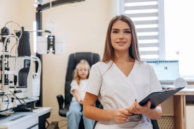 Elinde not defteriyle. Göz doktoru kliniğinde doktorla küçük bir kız..