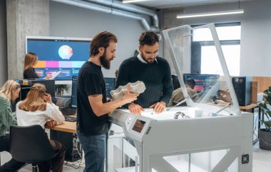 Çalışanlar bir arada. Ofiste 3D yazıcının yanında insanlar var..