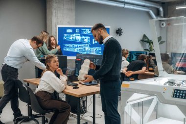 Çalışanlar bir arada. Ofiste 3D yazıcının yanında insanlar var..