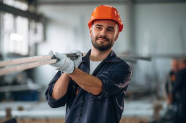 Metal parçaları, kalasları tutuyor. İnsanlar modern fabrikada çalışıyor..