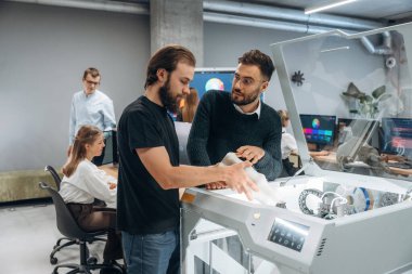 İletişim, bitmiş yazdırılmış nesne. Ofiste 3D yazıcının yanında insanlar var..