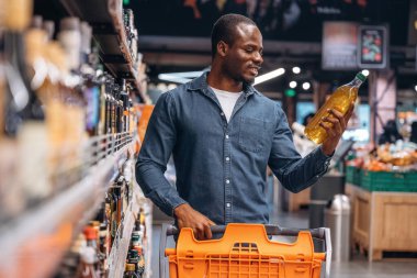 Ellerinde bir şişe sebze yağı. Erkek müşteri süpermarkette..