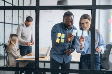 Fikirler camda, ayakta duruyor. Profesyonel işçiler modern ofiste birlikte çalışıyorlar..