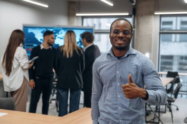 Afrikalı Amerikalı adam meslektaşlarına karşı duruyor. Bir grup ofis çalışanı içeride birlikte..