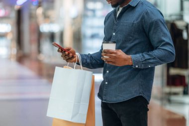 Akıllı telefon kullanıyor. Süpermarketteki alışveriş çantalı adamın yakın görüntüsü..