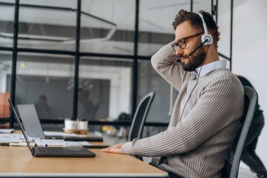 Kulaklıkla. Adam ofiste dizüstü bilgisayarın yanında oturuyor, iş kavramı..
