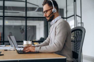 Kulaklıkla. Adam ofiste dizüstü bilgisayarın yanında oturuyor, iş kavramı..