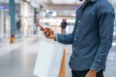 Akıllı telefondan interneti kaydırmak. Süpermarketteki alışveriş çantalı adamın yakın görüntüsü..