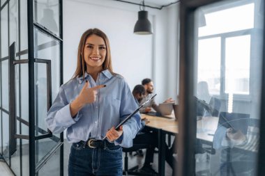 Kadın ayakta duruyor. Profesyonel işçiler modern ofiste birlikte çalışıyorlar..