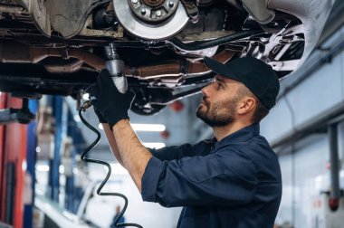 Otomobil çalışıyor, asılı. Araba tamirhanesinde çalışan bir tamirci..