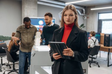 Dijital tablet ellerinde. Ofiste 3D yazıcının yanında insanlar var..