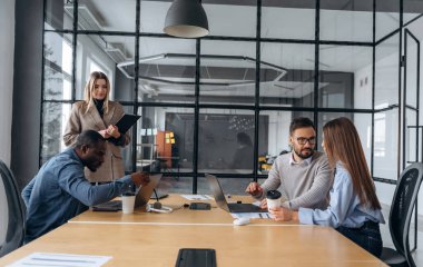 Sakin, masanın yanında oturuyor. Profesyonel işçiler modern ofiste birlikte çalışıyorlar..