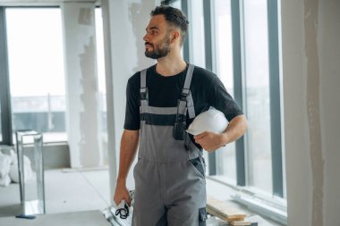 Gri üniformalı ve siyah gömlekli. Bir adam bitmemiş bir odayı yeniliyor..