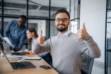 Plana göre, baş parmağını göstermek. Profesyonel işçiler modern ofiste birlikte çalışıyorlar..