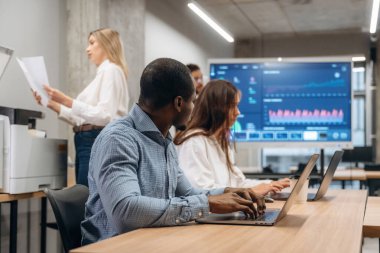 Dizüstü bilgisayarlar masada. Bir grup ofis çalışanı içeride birlikte..