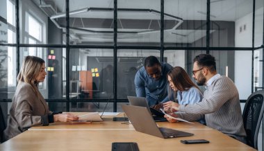 Sakin, masanın yanında oturuyor. Profesyonel işçiler modern ofiste birlikte çalışıyorlar..