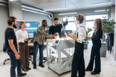 Çalışanlar bir arada. Ofiste 3D yazıcının yanında insanlar var..