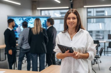 Bir kadının elinde not defteri. Bir grup ofis çalışanı içeride birlikte..