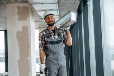 Tamirci, tavanda matkap ve metal parçaları taşıyor. Bir adam bitmemiş bir odayı yeniliyor..