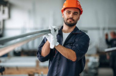 Metal parçaları, kalasları tutuyor. İnsanlar modern fabrikada çalışıyor..