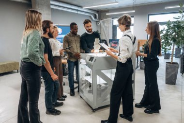 Toplanıyor, basılı ürünlere bakıyor. Ofiste 3D yazıcının yanında insanlar var..