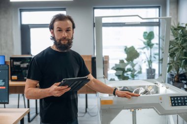 Ayakta, çalışıyor. Adam 3D yazıcıyla ofiste..