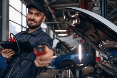 Tableti bağlamak için kablo. Araba tamirhanesinde çalışan bir tamirci..